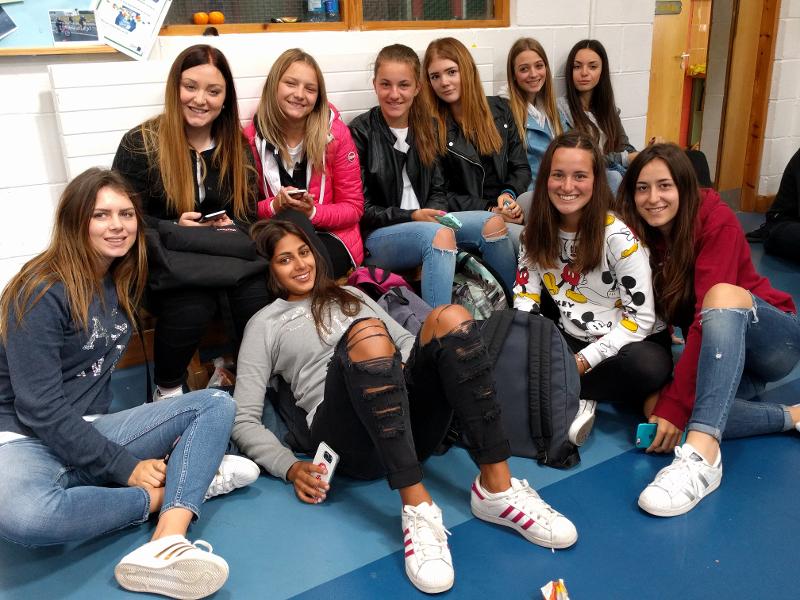 Un gruppo di ragazze siede insieme sorridendo in una stanza al campo estivo in tedesco
