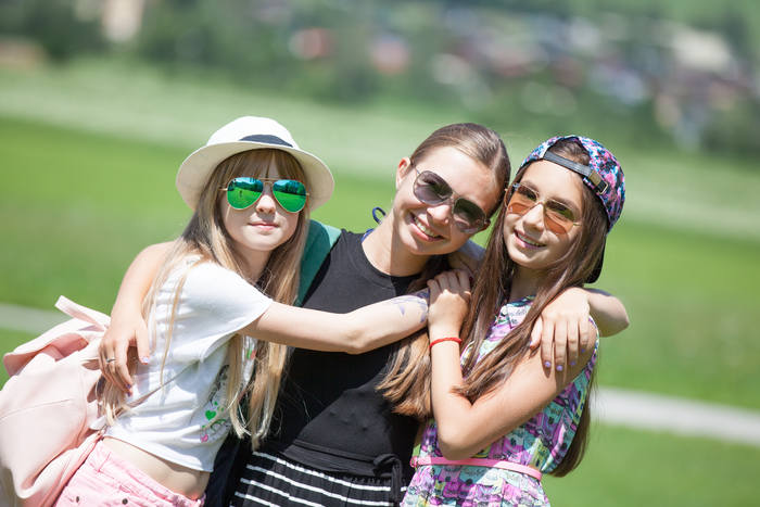 Durante il campo estivo in inglese tre ragazze con gli occhiali da sole si abbracciano