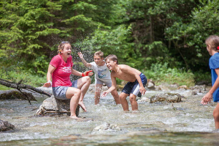 Al campo avventura in Austria i bambini al fiume schizzano l'istruttrice che è seduta su una roccia