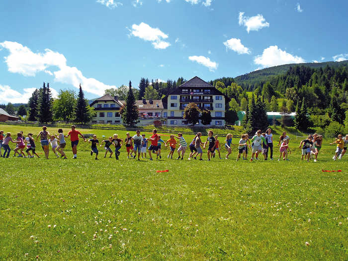Tanti bambini corrono insieme sul prato al campo avventura in Austria