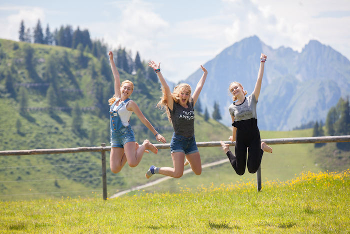 Al campo avventura in Austria tre ragazze saltano insieme e sorridono sul prato con dietro le montagne