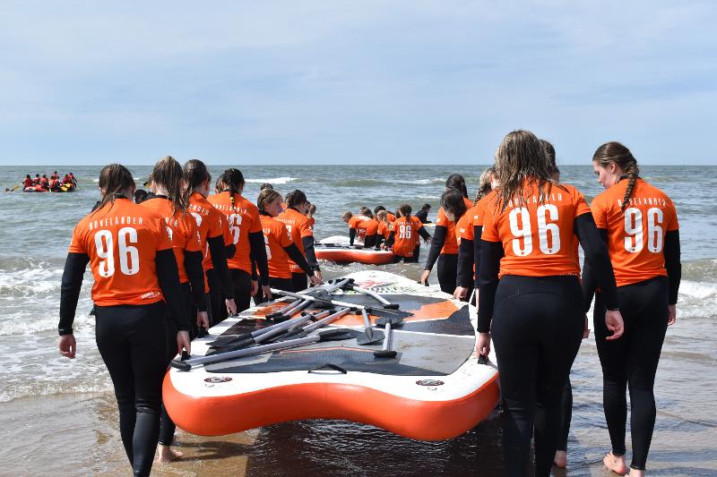 I partecipanti del campo estivo sport acquatici trasportano dei grandi SUP in mare