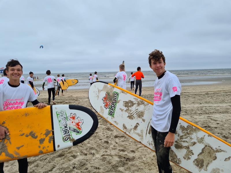 Tutti i partecipanti del campo estivo sport acquatici reggono una tavola da surf sotto il braccio