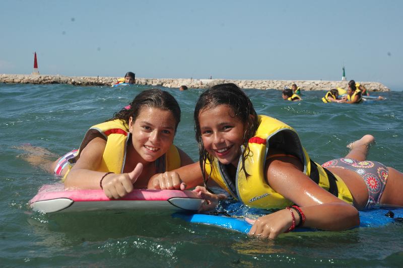 Durante il viaggio per ragazzi all'estero, due ragazze sorridenti galleggiano in mare sdraiate sopra a delle tavole da surf