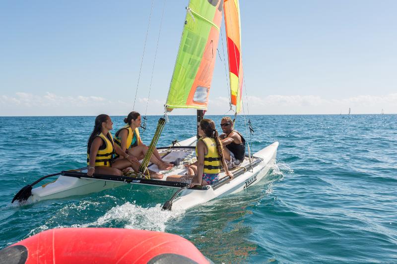 Durante il campo estivo Puglia, alcune ragazze sono in barca a vela con i giubbotti di salvataggio e con un istruttore