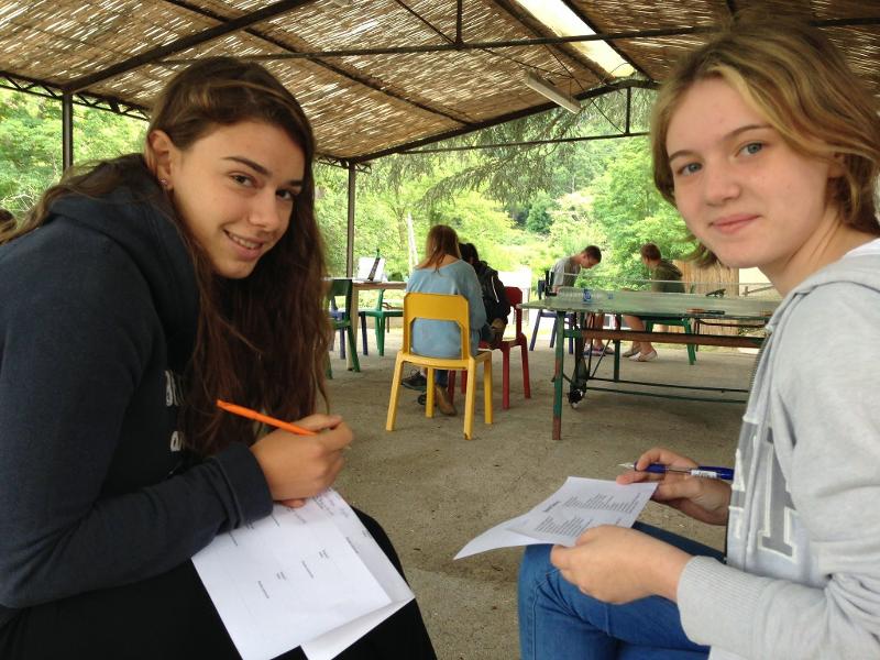 Al soggiorno linguistico in francese due ragazze sedute all'aperto sotto a un gazebo stanno scrivendo degli appunti
