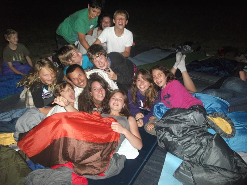 Un gruppo sorridente campeggia con i sacchi a pelo per terra durante la vacanza estiva per ragazzi