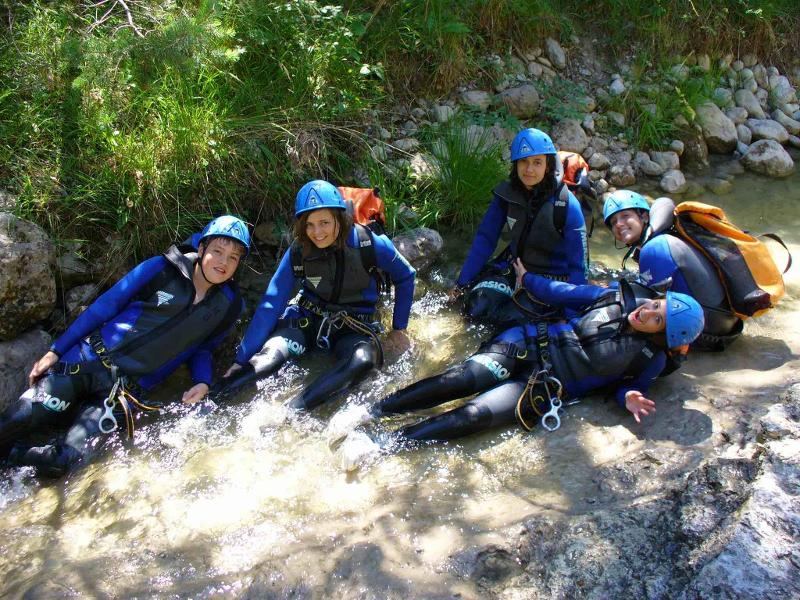 Cinque ragazzi della vacanza studio Francia sono sdraiati in un ruscello con indosso le mute da sub colore blu