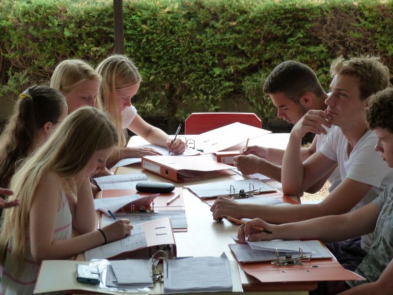 Alcuni ragazzi del soggiorno linguistico in francese sono seduti ad un tavolo all'aperto mentre studiano insieme la nuova lingua