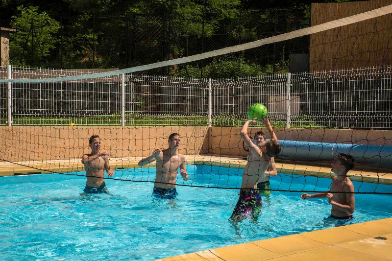 I ragazzi al soggiorno linguistico francese giocano a pallavolo in piscina con una palla verde e una rete nel mezzo