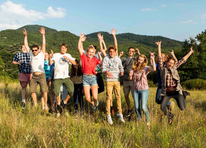 Il gruppo di ragazzi del soggiorno linguistico in francese sono in una campo con l'erba alta e saltano per la foto