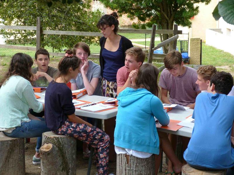 Al soggiorno linguistico francese i ragazzi seduti all'aperto studiano dai quaderni con un'insegnante