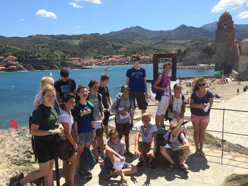 Il gruppo di ragazzi del soggiorno linguistico francese sono in posa per la foto davanti al porto sotto al sole e tengono in mano un foglio