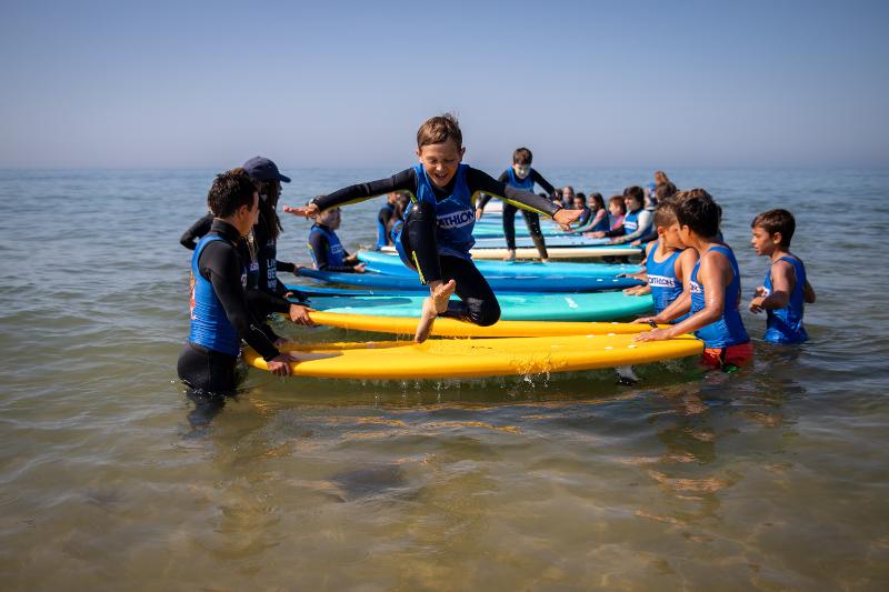 Ai surf camps Spagna un bambino corre e salta sopra a delle tavole da surf tenute da altri bambini