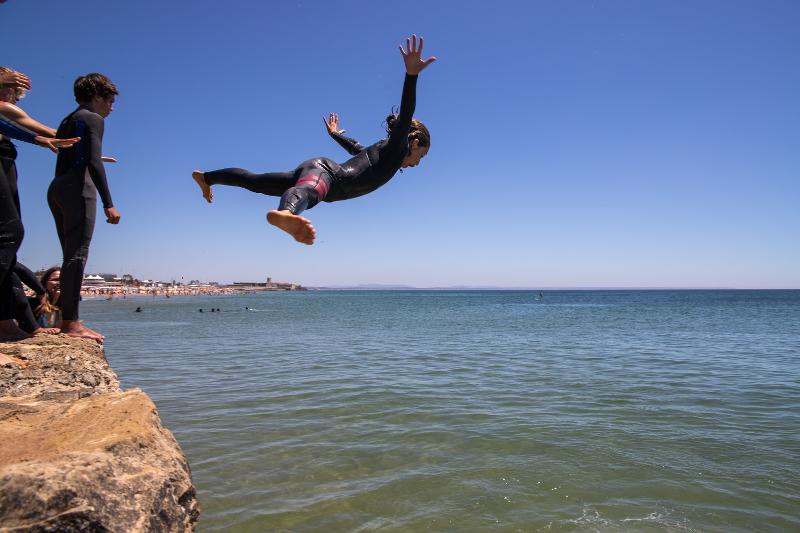 Ai surf camps Spagna un bambino fa un tuffo da una scogliera e gli altri bambini dietro di lui aspettano in fila