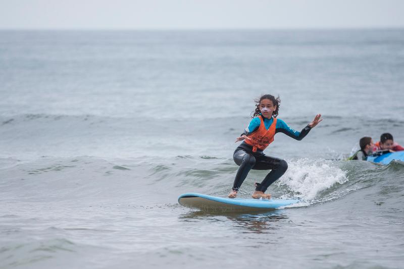 Una ragazza con la pittura bianca sul viso cavalca un'onda sulla tavola al campo estivo surf