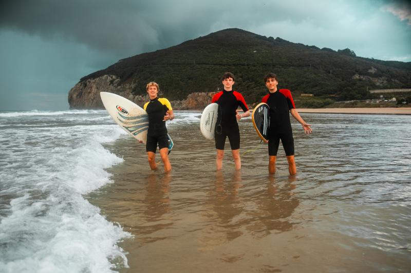 Alla Vacanza internazionale per ragazzi in Cantabria ci sono tre ragazzi in riva al mare con le loro tavole da surf pronti ad entrare in acqua