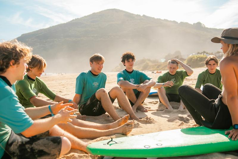Un istruttore parla sulla spiaggia ad un gruppo di partecipanti al campo estivo surf Lisbona
