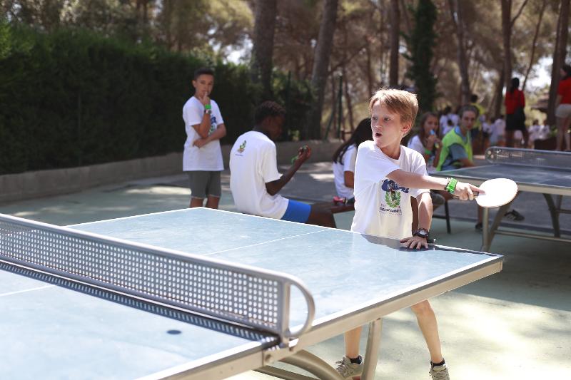 Un bambino concentrato a eseguire il colpo gioca a ping pong al campo estivo attività in Spagna
