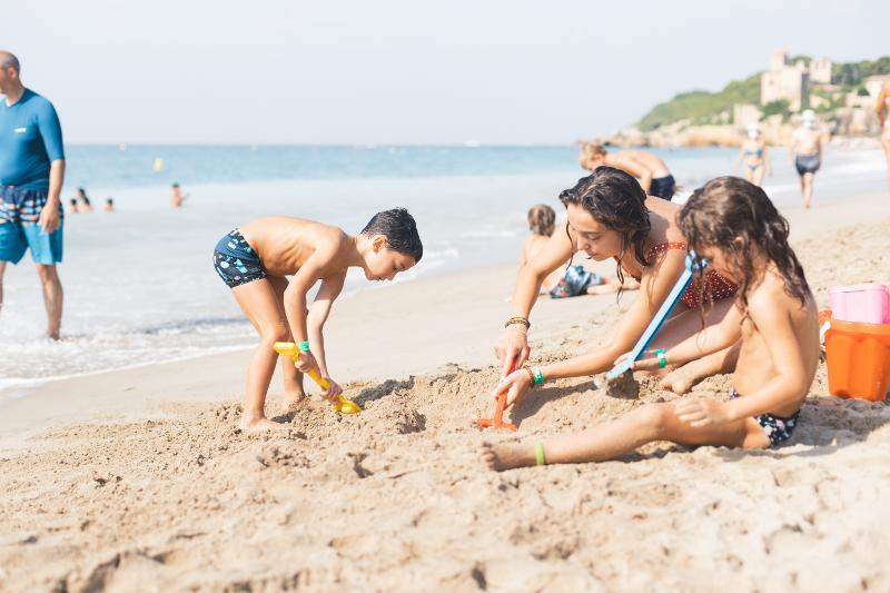 Tre bambini giocano con la sabbia e le palette mentre stanno in costume in riva al mare al campo estivo attività in Spagna