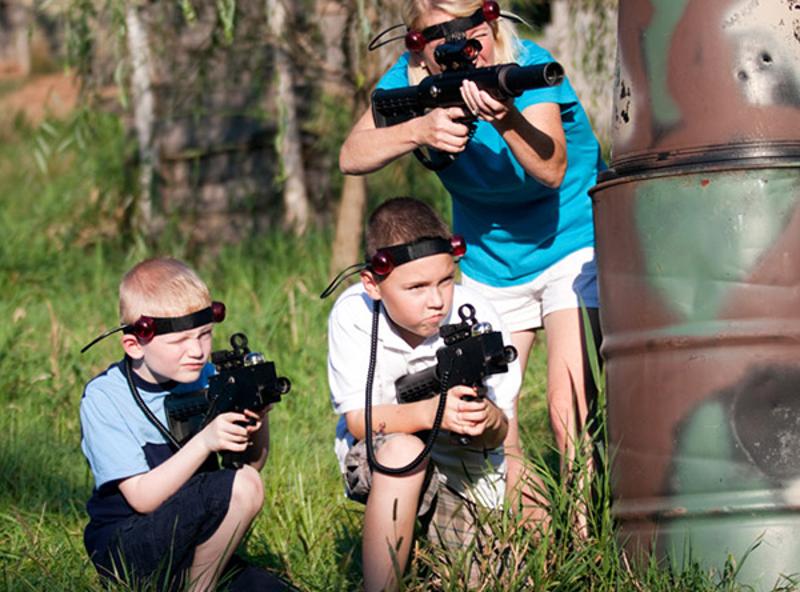 Al camp estivo tre ragazzi giocano a laser-tag e sono accucciati dietro a dei barili per protezione
