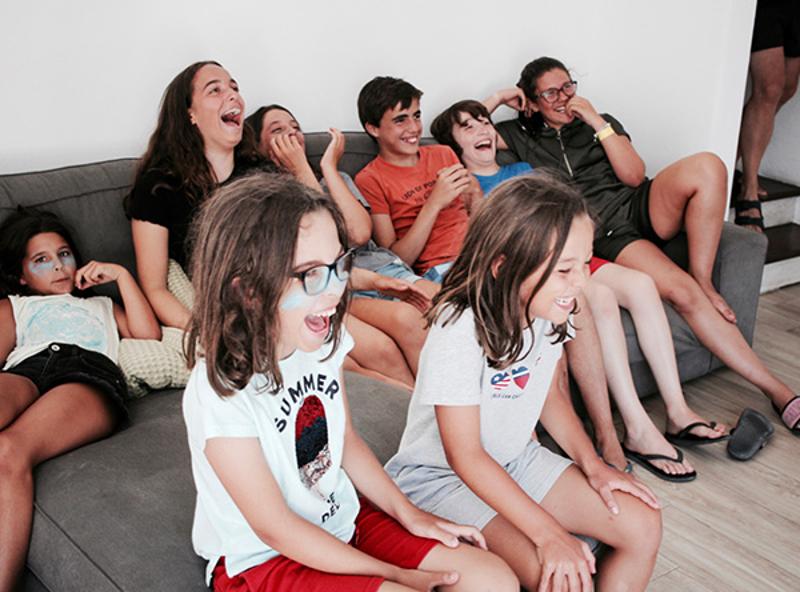 Un gruppo di otto ragazzi e ragazze ridono seduti sul divano grigio al camp estivo