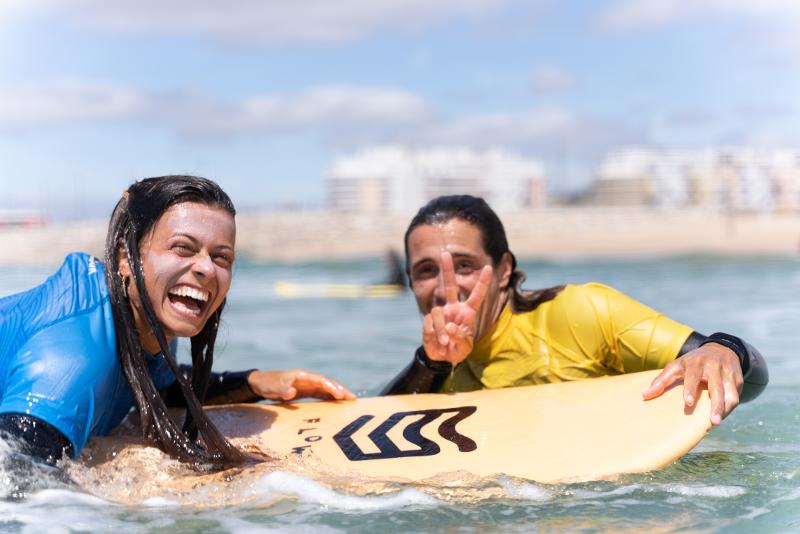 Due partecipanti dei surf camps Sardegna sorridono in acqua sulla tavola