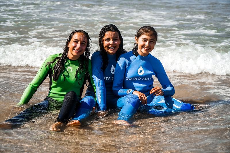 Nel campo estivo surf, tre ragazze con la tuta da surf siedono in riva al mare