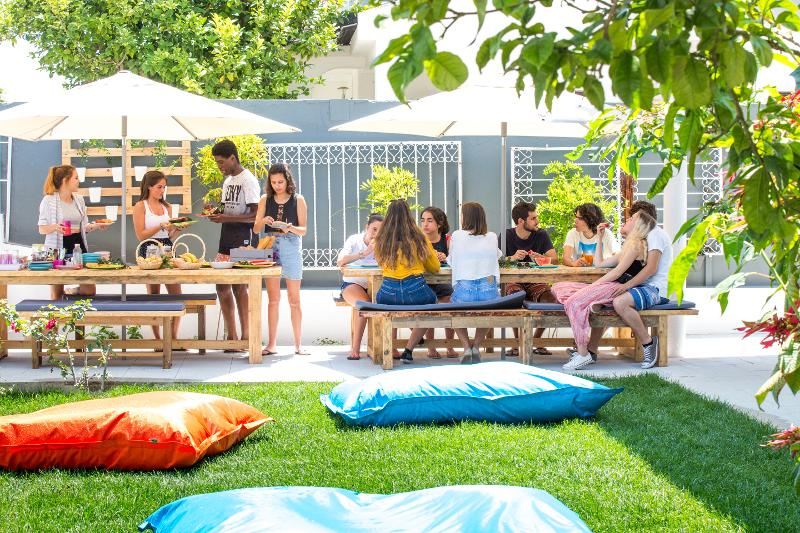 Un'estate di sole, surf e nuove amicizie ti aspetta al campo estivo surf! Due gruppi di partecipanti del campo estivo surf sono seduti sotto gli ombrelloni del giardino della residenza
