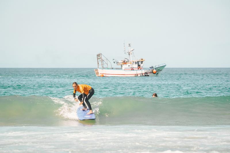 Un partecipante del campo estivo surf si alza in piedi sulla tavola ed è pronto a cavalcare l'onda