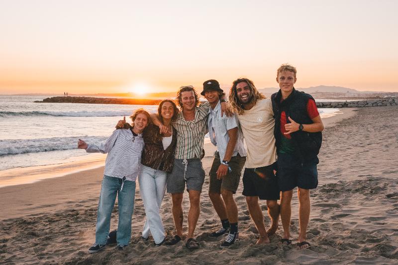 un gruppo di amici del campo estivo surf fa una foto di gruppo in spiaggia al tramonto