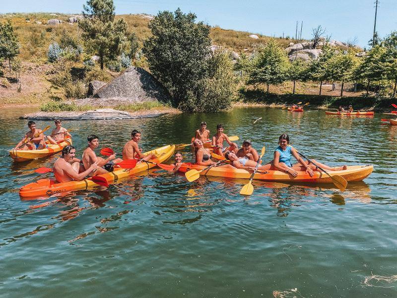 Ai campi estivi per ragazzi in Italia i ragazzi navigano l'acqua su delle canoe arancioni con i remi gialli