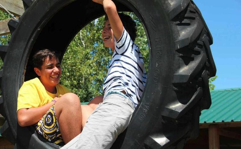 Due bambini del campo estivo inglese Bologna ridono mentre cercano di incastrarsi in una ruota gigante da trattore