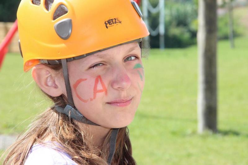 Al campo estivo Svezia una bambina con il viso pitturato e il casco arancione socchiude un occhio