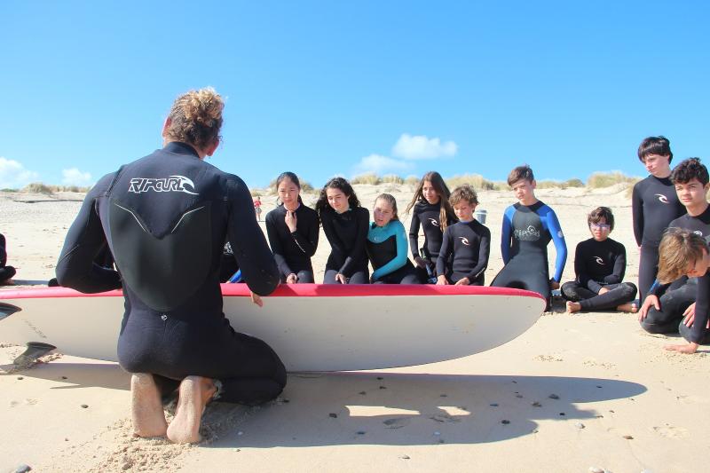 I bambini al campo estivo Sardegna seguono una lezione di surf tenuta da un istruttore professionista in spiaggia
