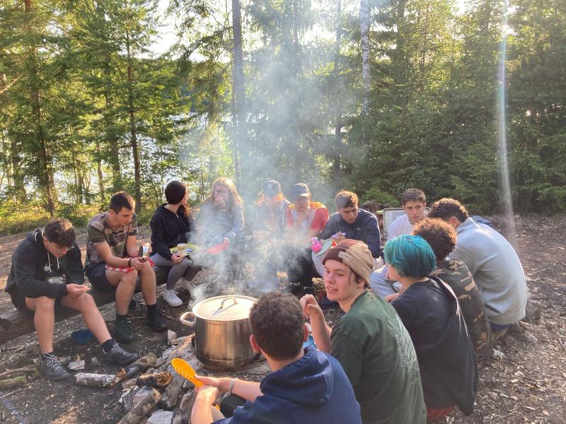Ragazzi del campo avventura in Svezia che mangiano intorno ad un pentolone sul fuoco