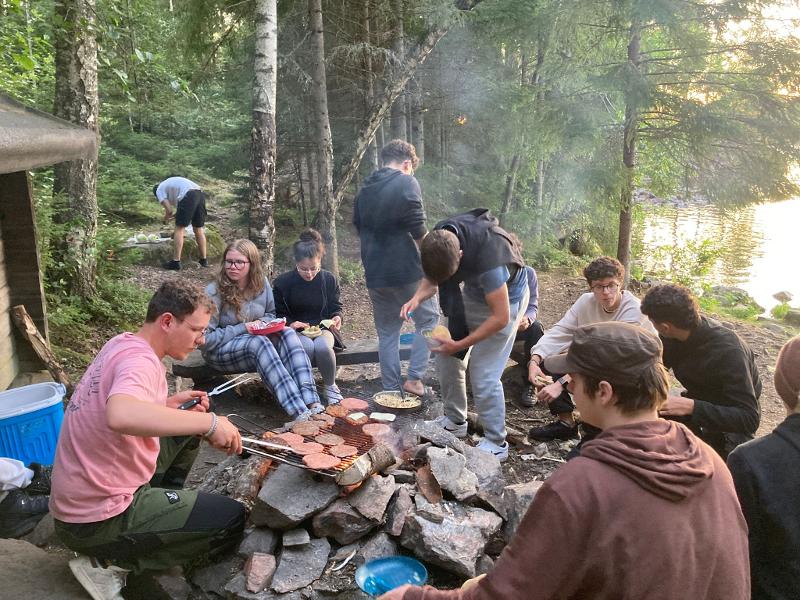 Un gruppo di ragazzi seduti a mangiare un barbecue intorno al fuoco al campo avventura