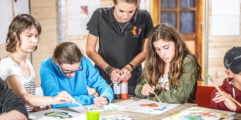 Alcuni ragazzi dipingono con acquerelli su un foglio con l'aiuto dell'insegnante del campo estivo motivazionale