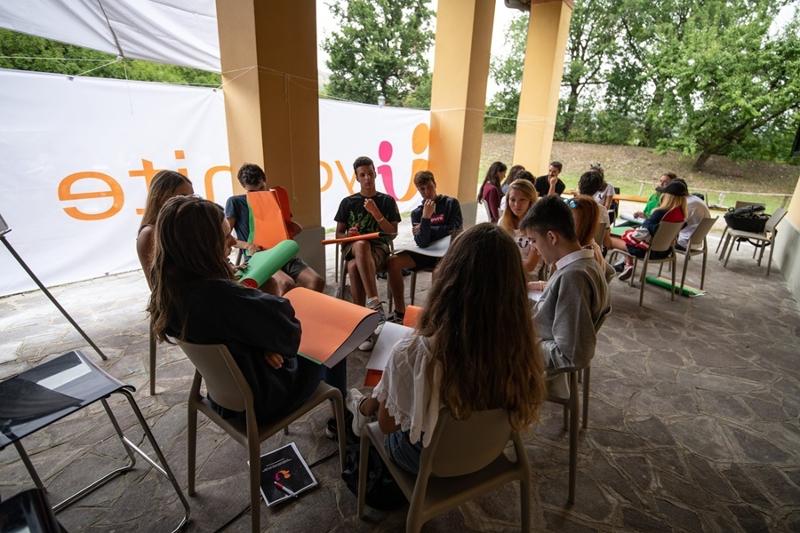 I ragazzi sono seduti in cerchio con dei cartoncini colorati a parlare durante il campo estivo inglese Toscana