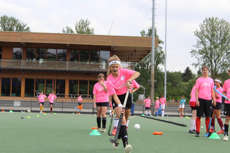 Una ragazza concentrata con la maglietta rosa corre con la mazza da hockey durante il campo estivo internazionale di Hockey a Rotterdam