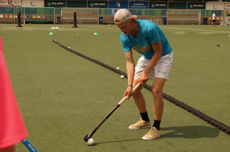 Un ragazzo con il cappellino bianco e la maglia azzurra si allena nella tecnica con la mazza da hockey al campo estivo internazionale di Hockey a Rotterdam
