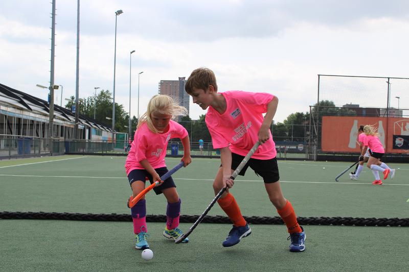 Due bambini con la divisa rosa cercano di ottenere la palla da hockey al estivo internazionale di Hockey a Rotterdam