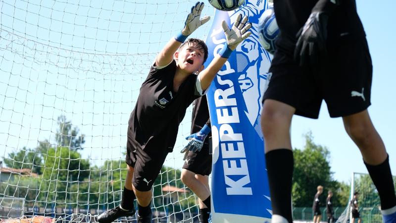 Un bambino partecipante al campus estivo calcio respinge un pallone con forza e tecnica