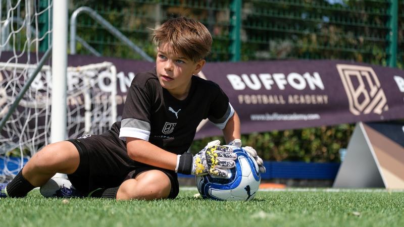 Un giovane portiere del campus estivo calcio si rialza con la palla in mano a seguito di una parata