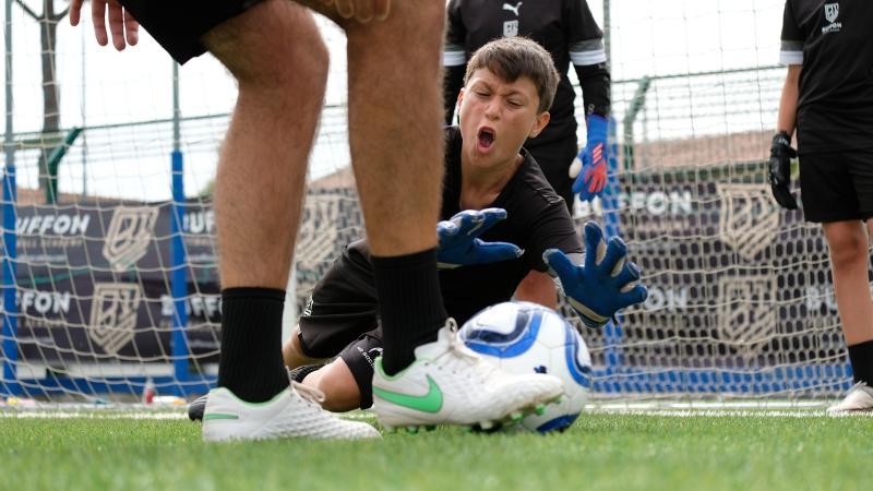 Un portiere del campus estivo calcio si tuffa per respingere un pallone che sta per essere calciato
