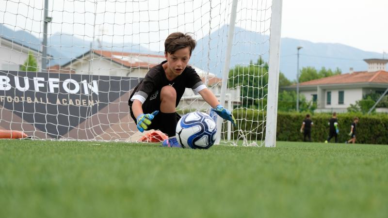 Un bambino partecipante al campus estivo calcio si accinge al tuffo per parare un pallone già in movimento