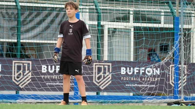 Un giovane portiere del campus estivo calcio osserva attentamente i suoi compagni giocare mentre protegge la porta