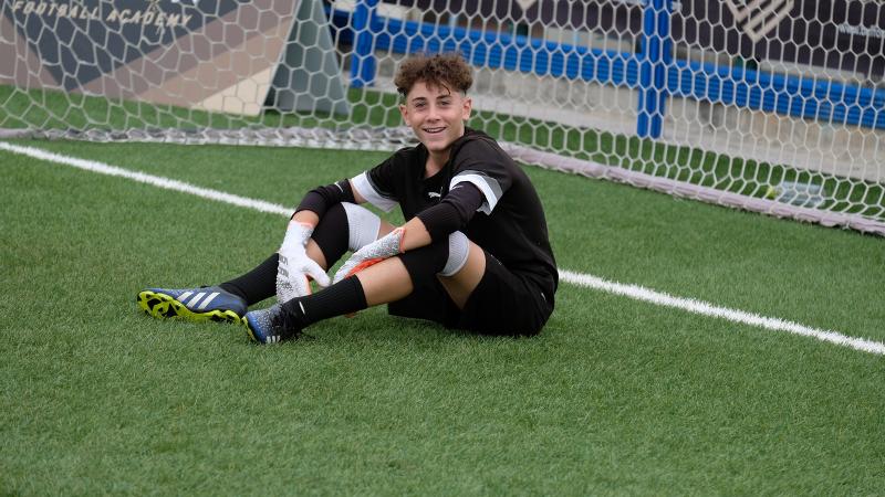 Un partecipante al campus estivo calcio è felice e seduto sulla linea di fondo davanti alla porta 