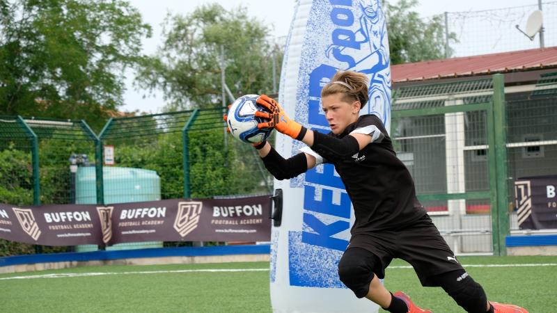 Un ragazzo del campous estivo calcio blocca un tiro in tuffo davanti a uno strumento propedeutico all'allenamento