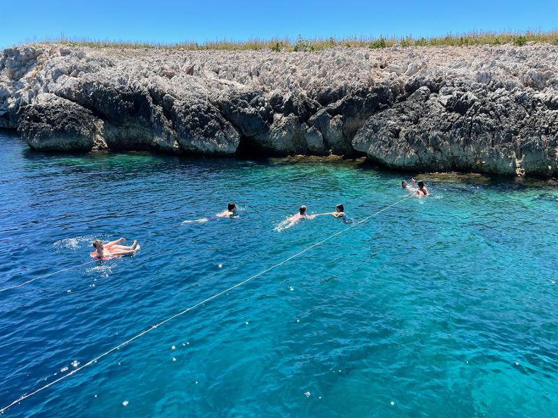Al campo estivo Marche, i ragazzi stanno nuotando nel mare azzurro con dei salvagenti vicino a una costa